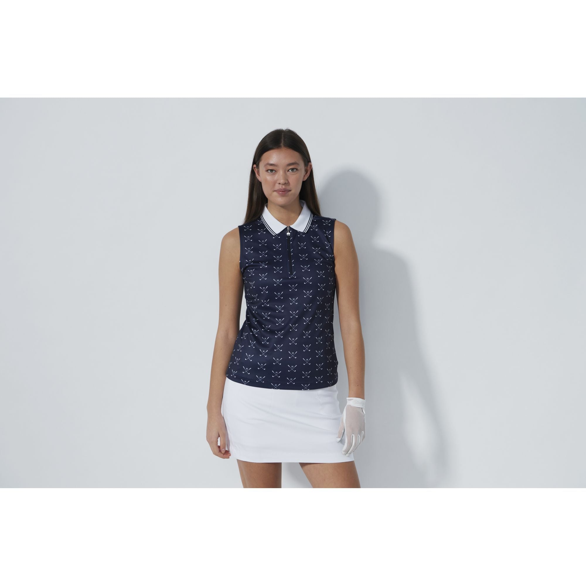A woman wearing a sleeveless Daily Sports Golf Polo with a patterned design in blue and white, paired with a white skirt and golf gloves.