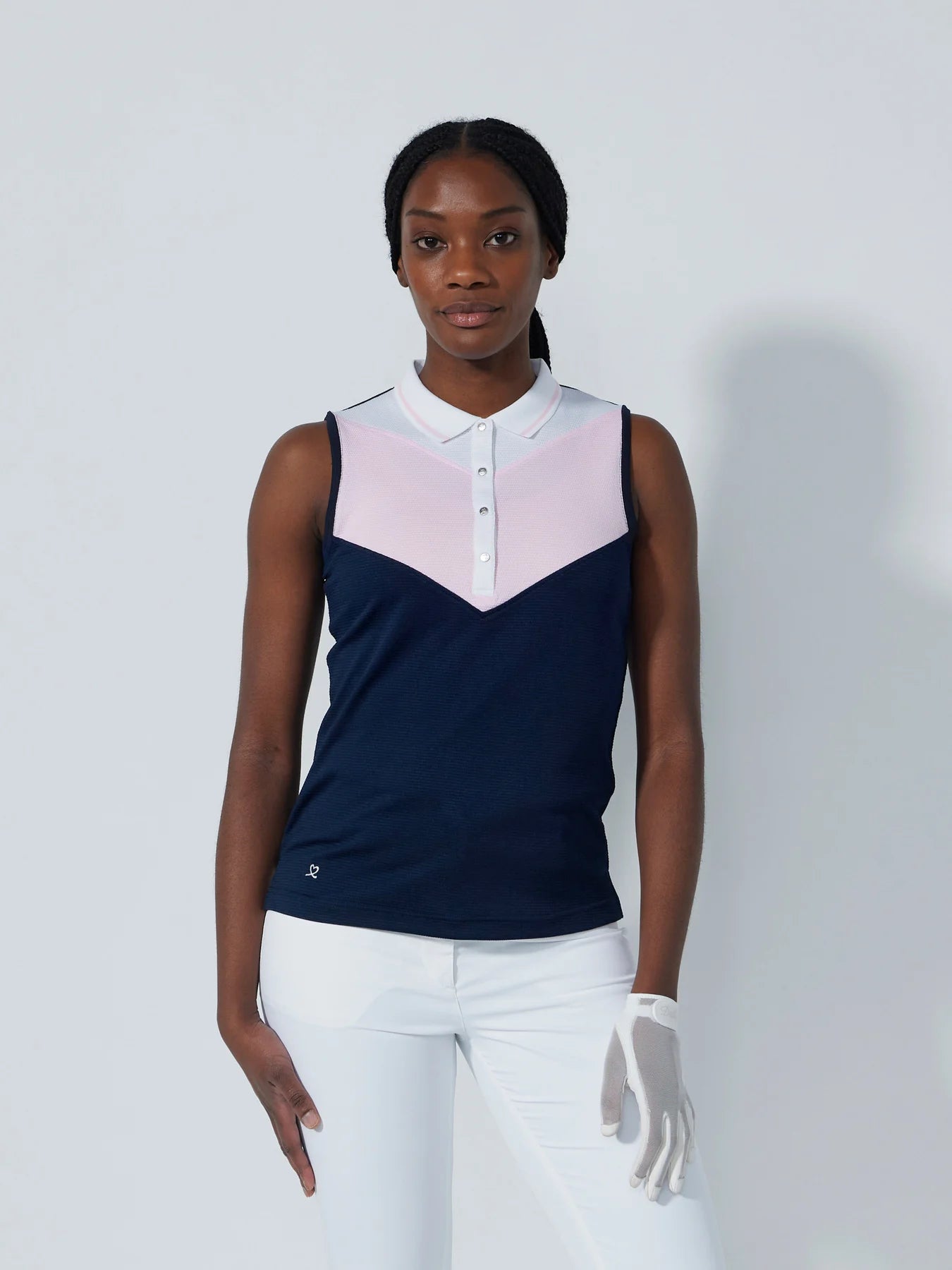 A woman wearing a sleeveless Daily Sports Match polo in navy blue with white and pink accents, designed for golf.