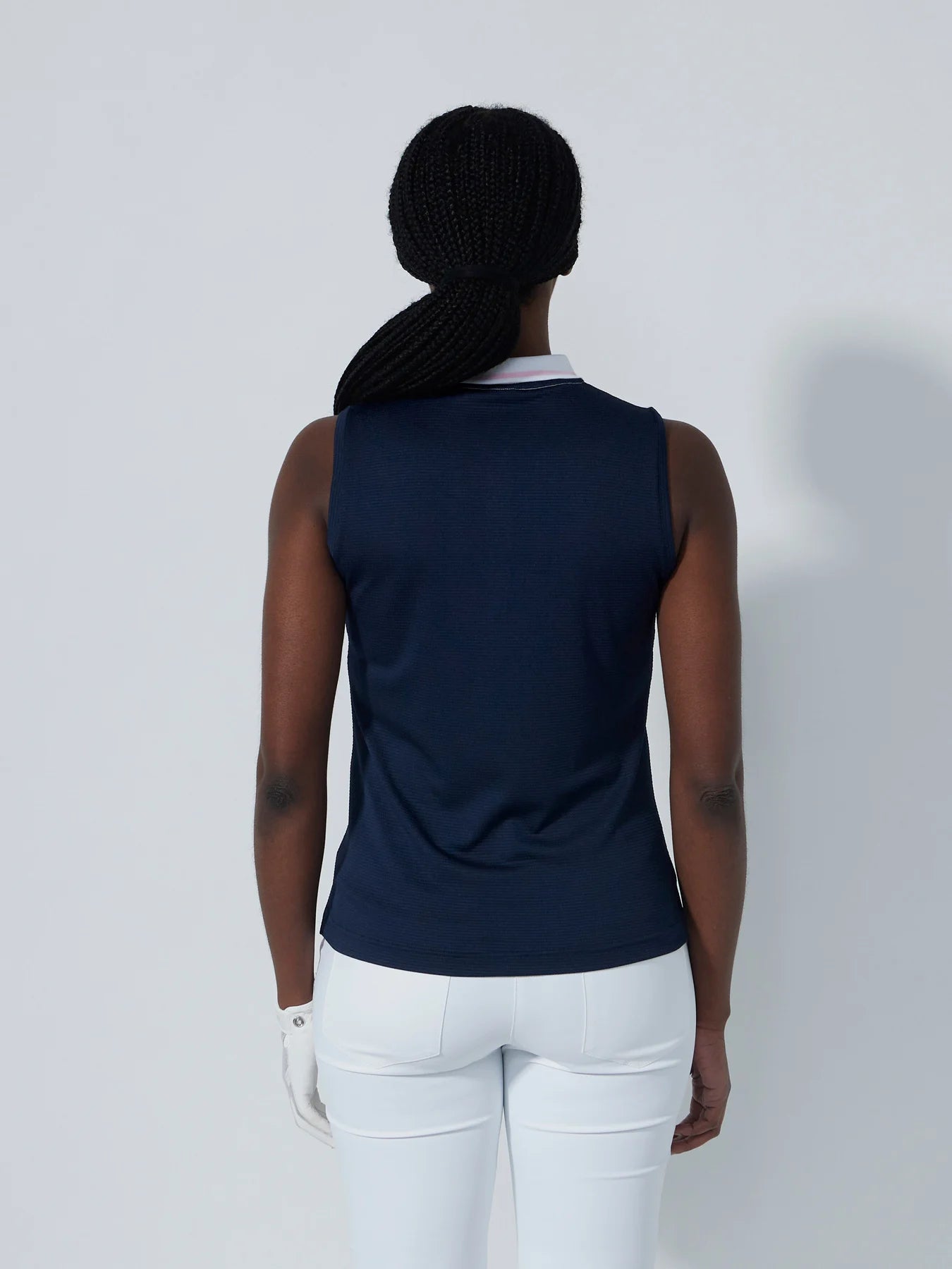 A woman wearing a sleeveless Daily Sports Match polo in navy blue with white and pink accents, designed for golf.