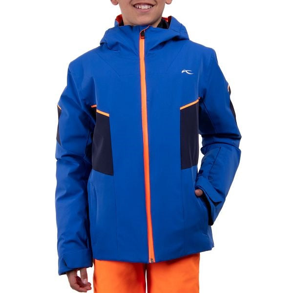 A boy wearing a blue Kjus Boy's Formula Ski Jacket that features a 20K waterproof and 20K breathable membrane, and a premium 4-way stretch fabric.