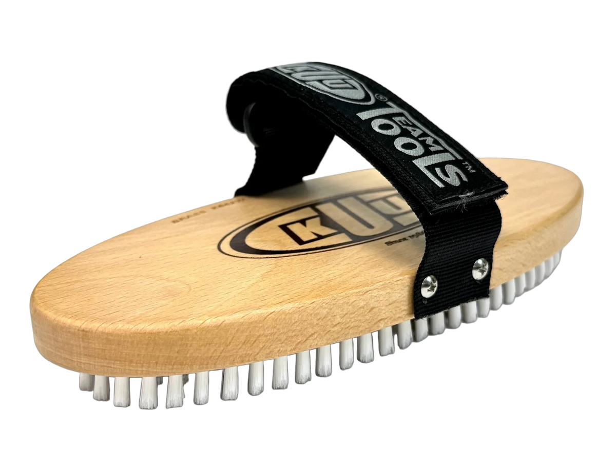 A Kuu Oval Brass Brush showing a curved wooden block base set with fine metallic wire bristles and an adjustable fabric hand strap across the top surface.