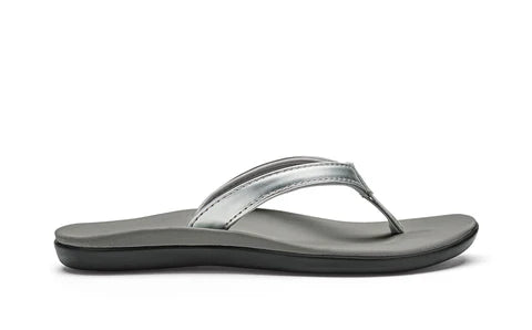A silver Olukai Junior Girls Ho'opio flip-flop sandal with a grey sole on a white background