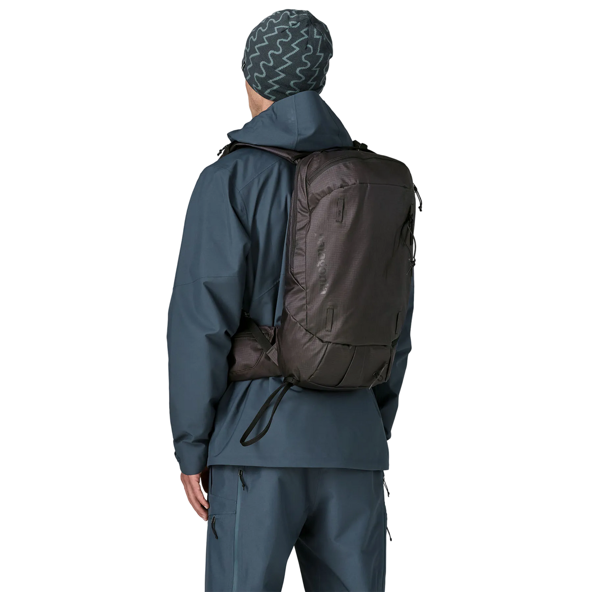 Rear view of a black Patagonia SnowDrifter Pack 20L featuring weather-resistant recycled nylon ripstop fabric, diagonal ski and vertical snowboard carry loops, a front avalanche safety gear pocket, fleece-lined top goggle pocket, and shoulder harness accessory pockets.