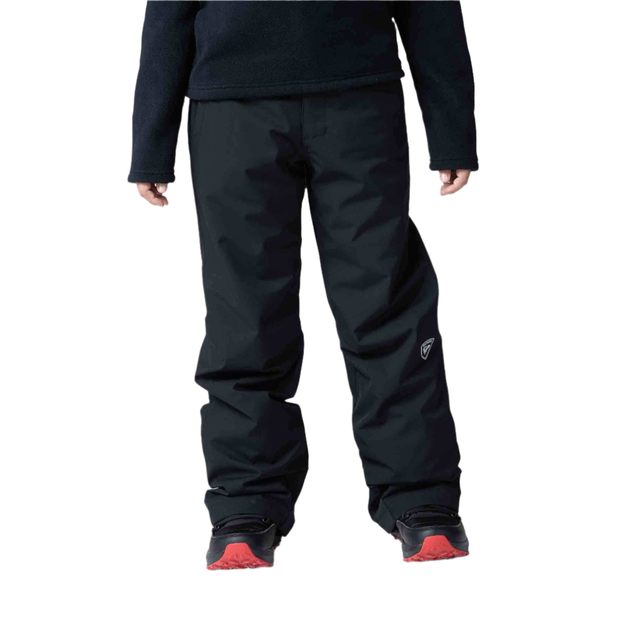 A boy wearing a pair of black Rossignol Boys' Ski Pants that are waterproof, breathable, stretchable, and insulated.