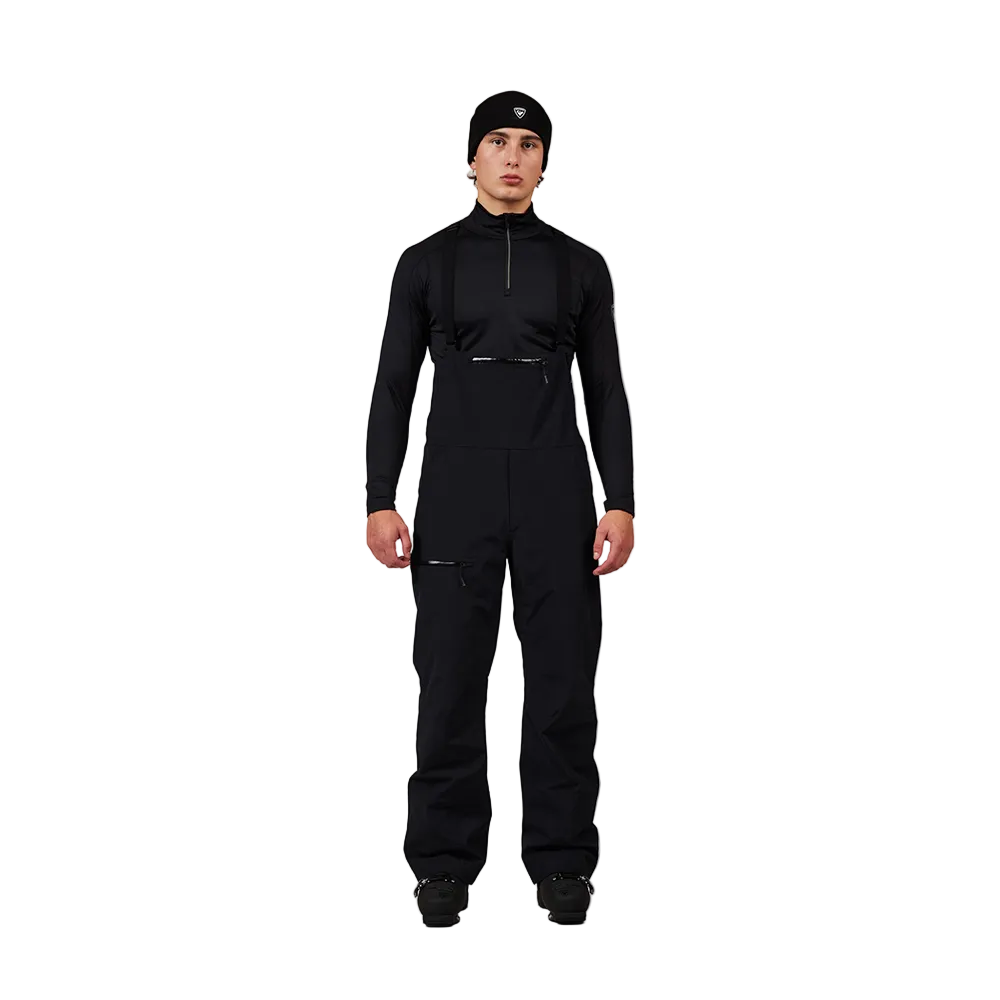 Front view of black Rossignol Men’s Outerlimits Insulated Bib Pants featuring high-chest bib construction, waterproof membrane fabric, adjustable shoulder suspenders, zippered thigh vents, integrated boot gaiters, and reinforced hem scuff guards.