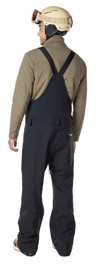 A man wearing a pair of black Rossignol Men's SKPR 3L AYR Bib Pants that are waterproof, breathable, stretchable, and warm.