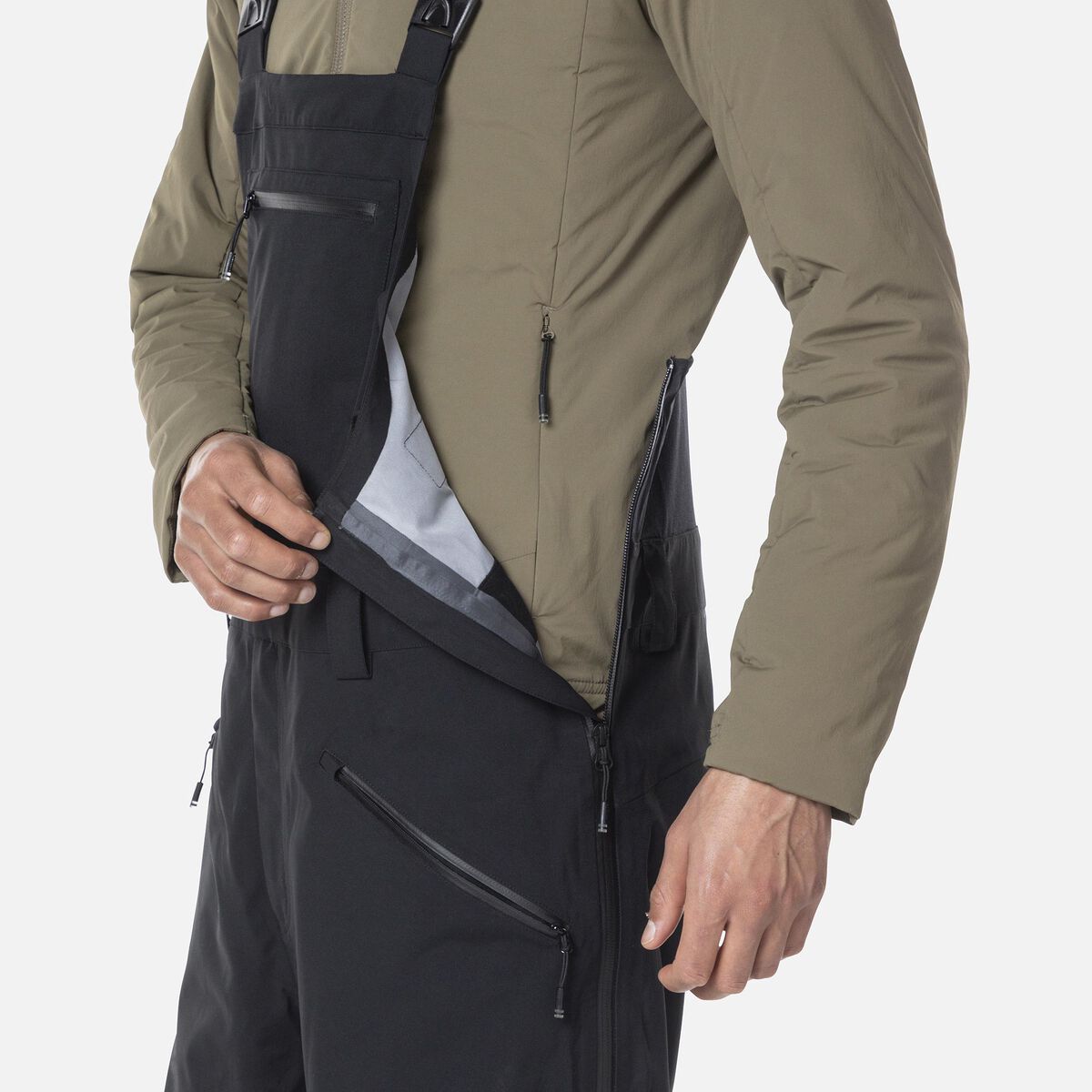 A close-up of a man wearing a pair of black Rossignol Men's SKPR 3L AYR Bib Pants that are waterproof, breathable, stretchable, warm, and include vents.