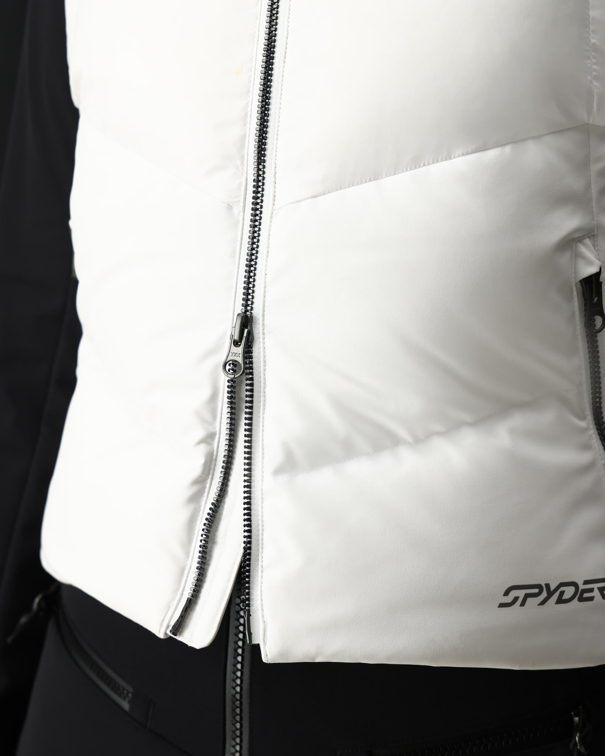 A close-up of a woman wearing a white Spyder Women's Eastwood Down Vest that is waterproof, breathable, stretchable, and insulated with down.