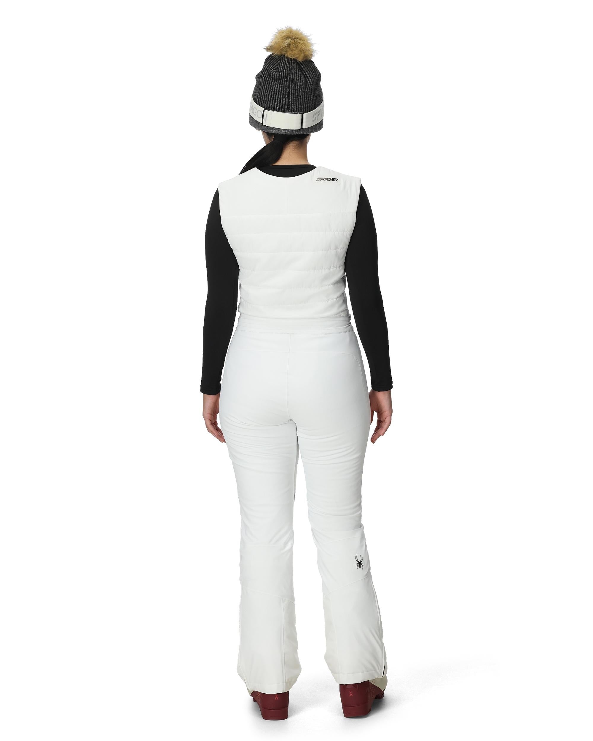 A woman wearing a pair of white Spyder Women's On Piste Ski Bib Pants which are waterproof, breathable, stretchable, and insulated.