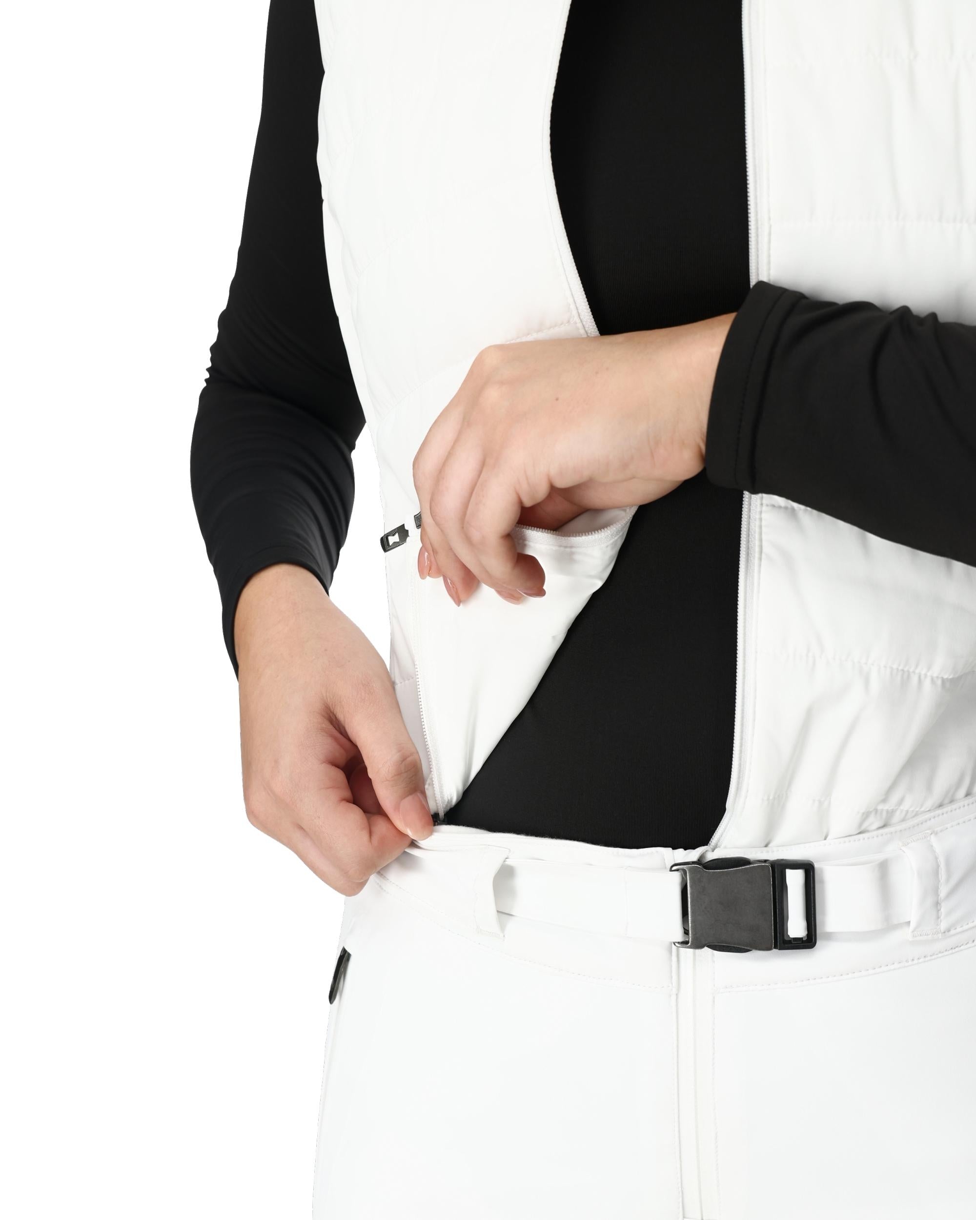 A woman wearing a pair of white Spyder Women's On Piste Ski Bib Pants which are waterproof, breathable, stretchable, and insulated.