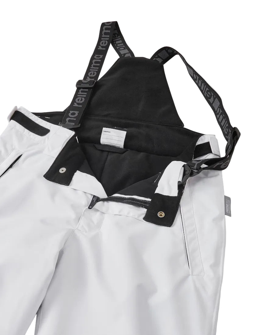Close-up view of white Reima Jr Terrie Pants featuring a waterproof Reimatec shell, detachable elastic suspenders, reinforced ankle scuff guards, and internal snow gaiters.