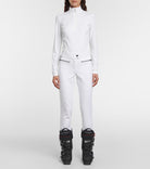 A woman wearing a white Bogner Women's Medita T-Neck sweater that features quick-drying, moisture-wicking, stretchable technical fabric in a slimming, fashionable silhouette.