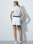 A woman wearing a white Daily Sports Women's Pescara 18" Golf Skort against a white background