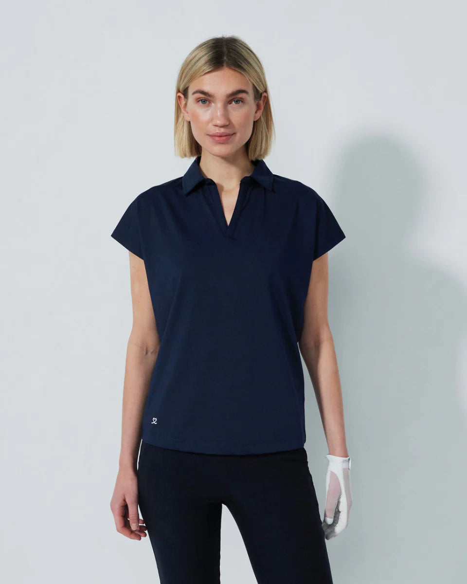 Woman wearing a navy blue Daily Sports Bella Birdie Cap Sleeve polo shirt against a light gray background