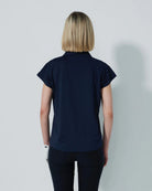 Woman wearing a navy blue Daily Sports Bella Birdie Cap Sleeve polo shirt against a light gray background