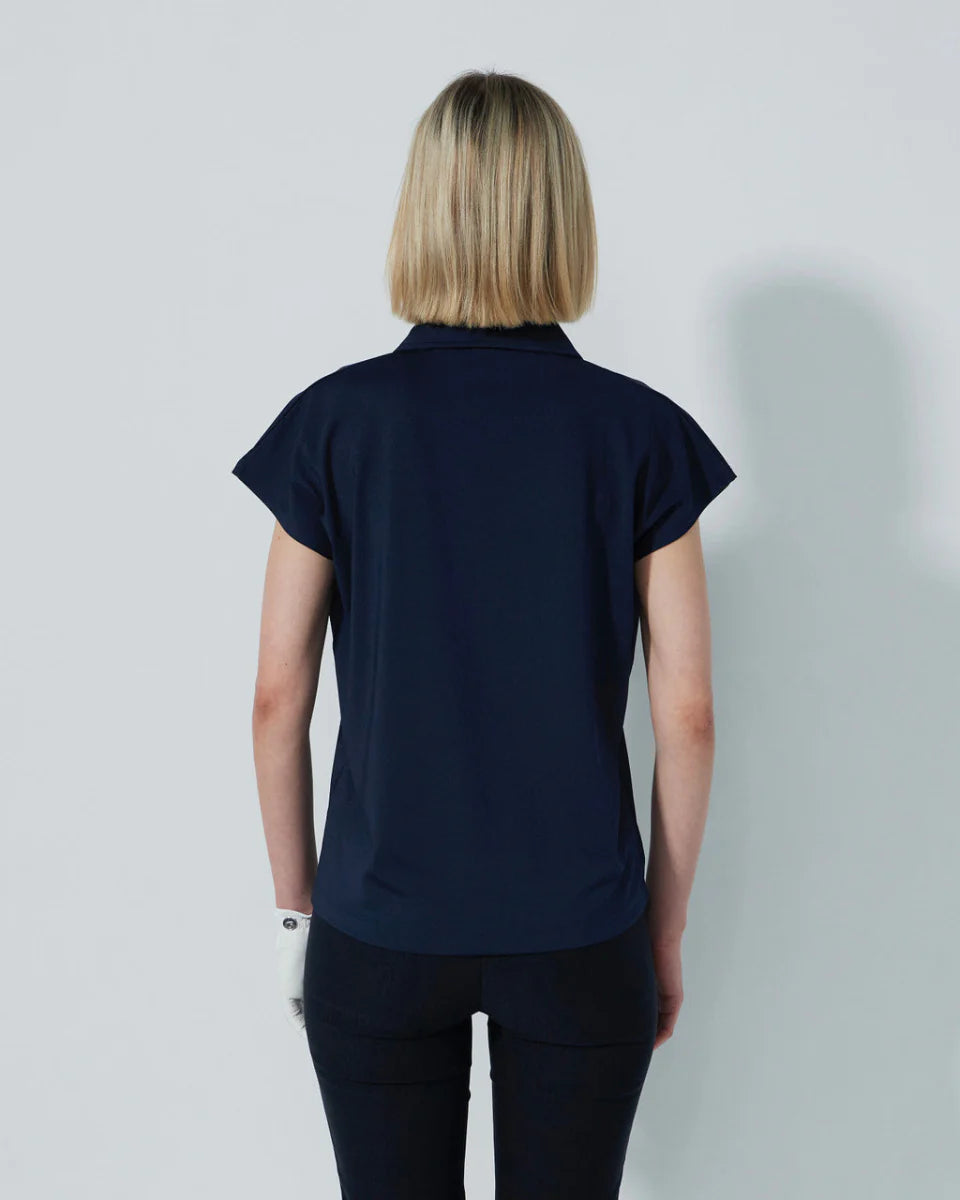 Woman wearing a navy blue Daily Sports Bella Birdie Cap Sleeve polo shirt against a light gray background