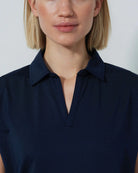 Woman wearing a navy blue Daily Sports Bella Birdie Cap Sleeve polo shirt against a light gray background