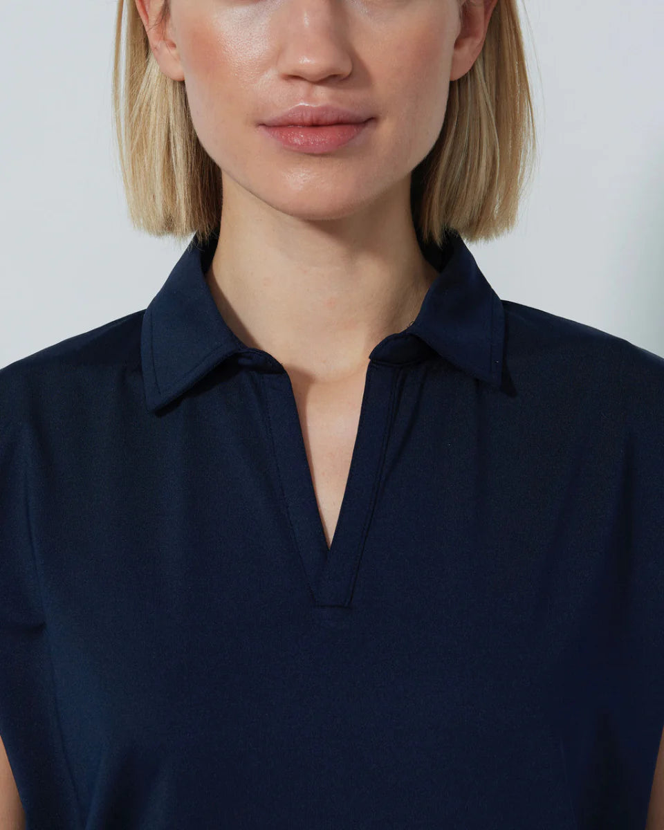 Woman wearing a navy blue Daily Sports Bella Birdie Cap Sleeve polo shirt against a light gray background