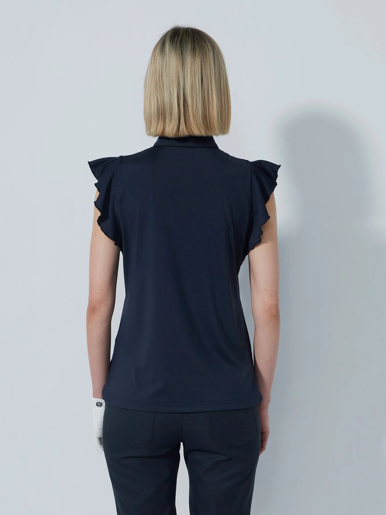 A woman wearing a navy Daily Sports Women's Luxe sleeveless polo shirt with ruffled cap sleeves and a collar.