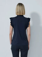 A woman wearing a navy Daily Sports Women's Luxe sleeveless polo shirt with ruffled cap sleeves and a collar.