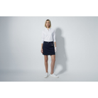 A woman wearing a white Daily Sports shirt and navy Daily Sports golf skort standing against a grey background.