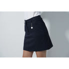 A woman wearing a white Daily Sports shirt and navy Daily Sports golf skort standing against a grey background.