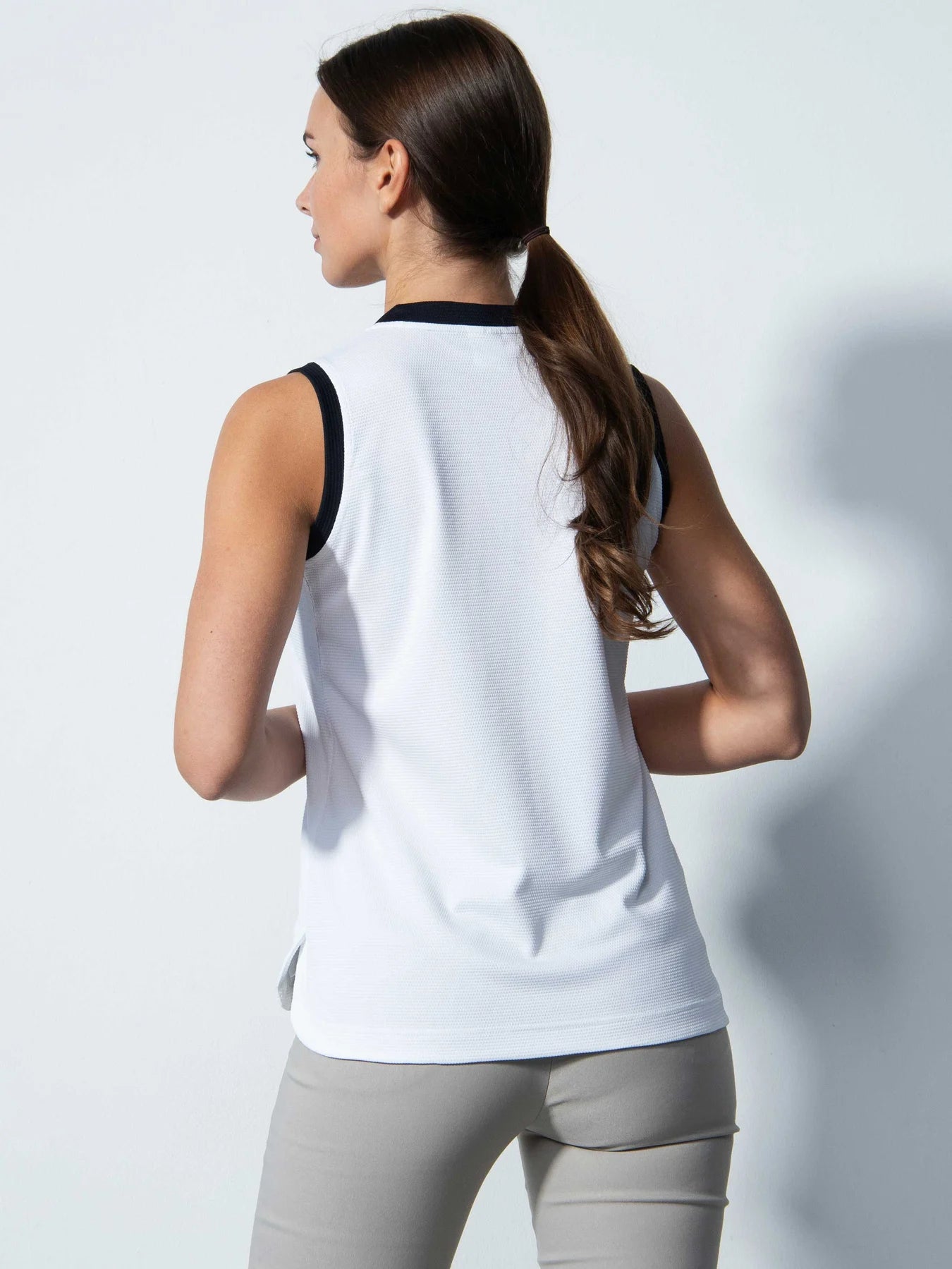 A woman wearing a white Daily Sports Women's Massy Sleeveless Polo Shirt on a white background