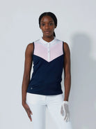 A woman wearing a sleeveless Daily Sports Match polo in navy blue with white and pink accents, designed for golf.