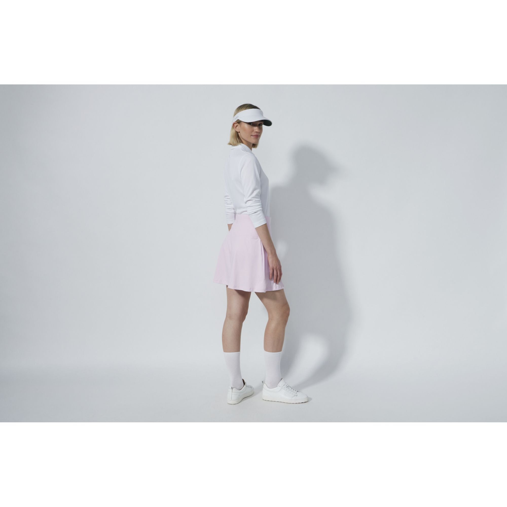 A woman wearing a white Daily Sports top and a purple Daily Sports skort with white golf shoes and a visor.
