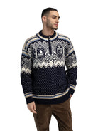 A man wearing a navy and off-white Dale of Norway Men's VM Trondheim Sweater which features Scandinavian-inspired geometric patterns and is made from luxurious 100% Norweigan merino wool.