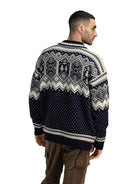 A man wearing a navy and off-white Dale of Norway Men's VM Trondheim Sweater which features Scandinavian-inspired geometric patterns and is made from luxurious 100% Norweigan merino wool.