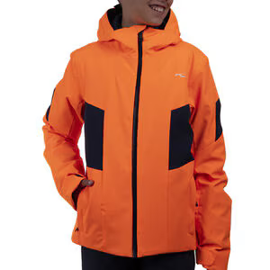 A boy wearing an orange Kjus Boy's Formula Ski Jacket that features a 20K waterproof and 20K breathable membrane, and a premium 4-way stretch fabric.