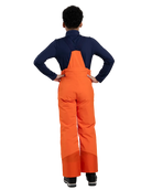 Rear view of orange Kjus Jr Boys’ Vector Max Pants featuring 2-layer waterproof fabric, Fast Thermo Core insulation, water-repellent zippers, reinforced scuff guards, and the KJUS-GROW leg extension system.