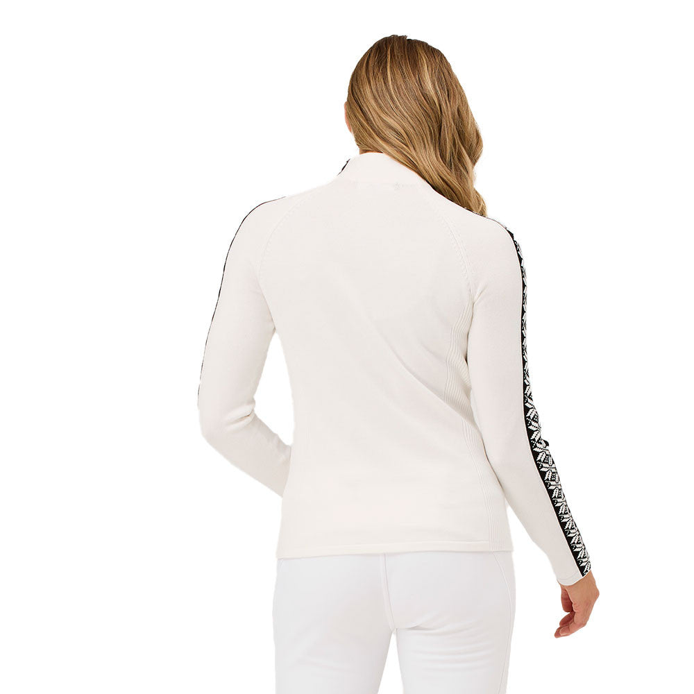 A woman wearing a white Krimson Klover Women's Slalom Zip Neck Sweater with black snowflake jacquard sleeve details and a quarter zip front.