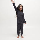 A child wearing a pair of black Le Bent Kids' Core Midweight Baselayer Bottoms that are stretchable, breathable, and made from a premium bamboo and merino wool blend.