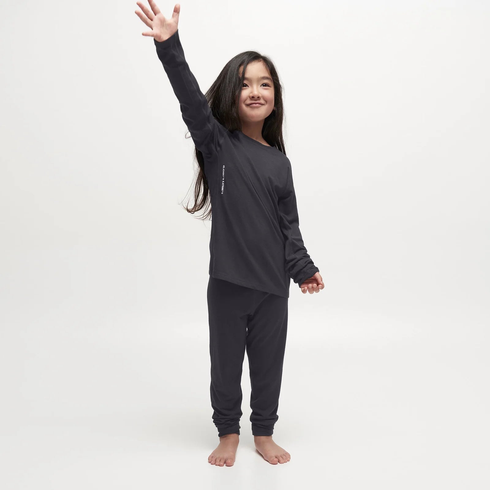 A child wearing a pair of black Le Bent Kids' Core Midweight Baselayer Bottoms that are stretchable, breathable, and made from a premium bamboo and merino wool blend.