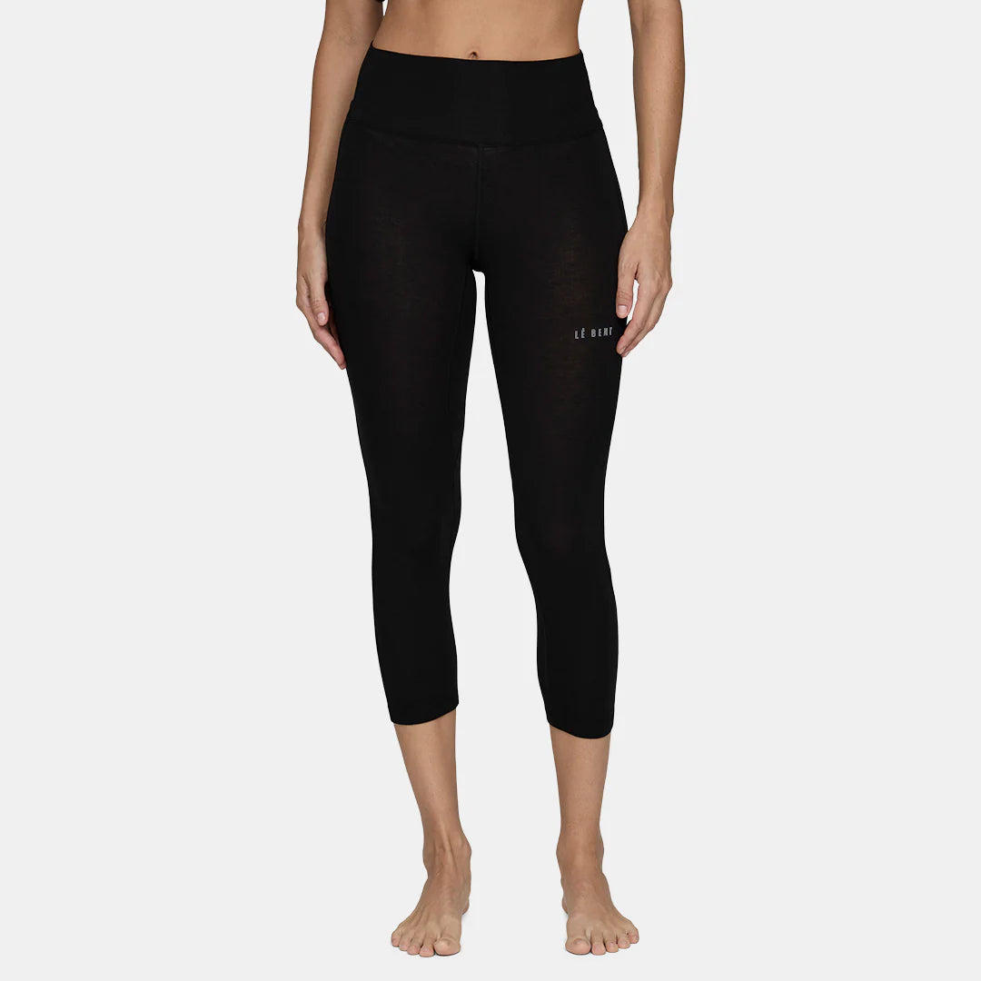 A woman wearing a pair of black Le Bent Women's Core Lightweight 3/4 Baselayer Bottoms which are designed to pair with ski boots and snowboard boots to keep you warm in harsh winter conditions.