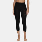 A woman wearing a pair of black Le Bent Women's Core Lightweight 3/4 Baselayer Bottoms which are designed to pair with ski boots and snowboard boots to keep you warm in harsh winter conditions.