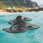 A pair of black Olukai Men's Ohana flip-flop sandals with an Olukai logo floating on water
