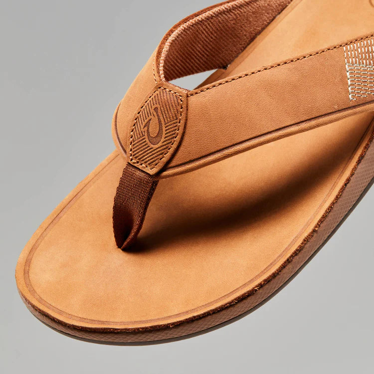 A brown leather Olukai Men's Tuahine flip-flop sandal on a white background