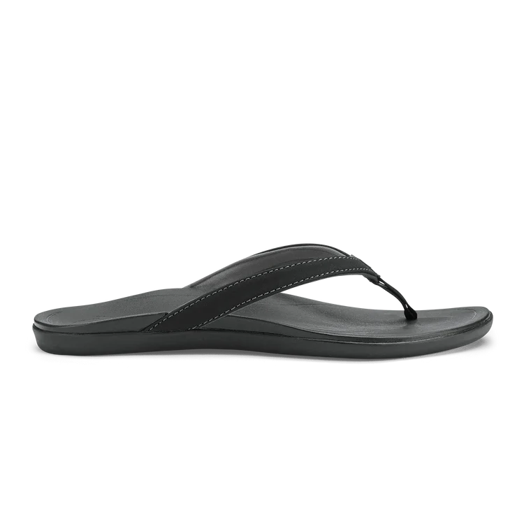 A black Olukai Women's Ho'opio flip-flop sandal on a white background