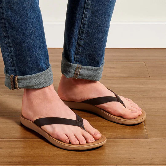 A woman wearing a pair of brown leather Olukai Women's Nonohe flip-flop sandals