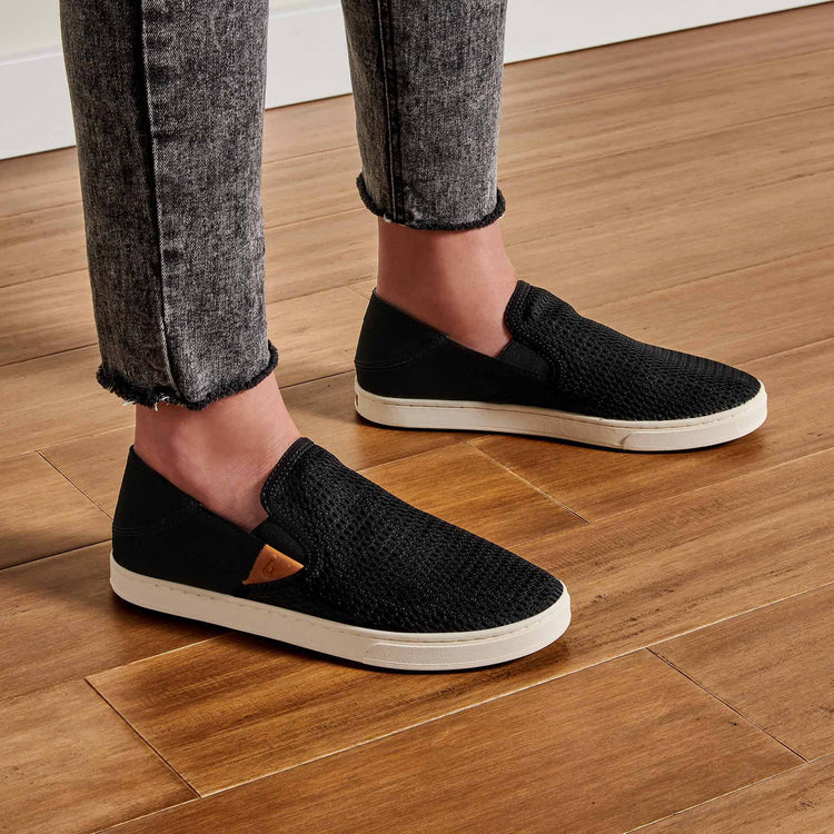 Black Olukai Women's Pehuea slip-on shoes that features a collapsible heel with a white sole on a white background