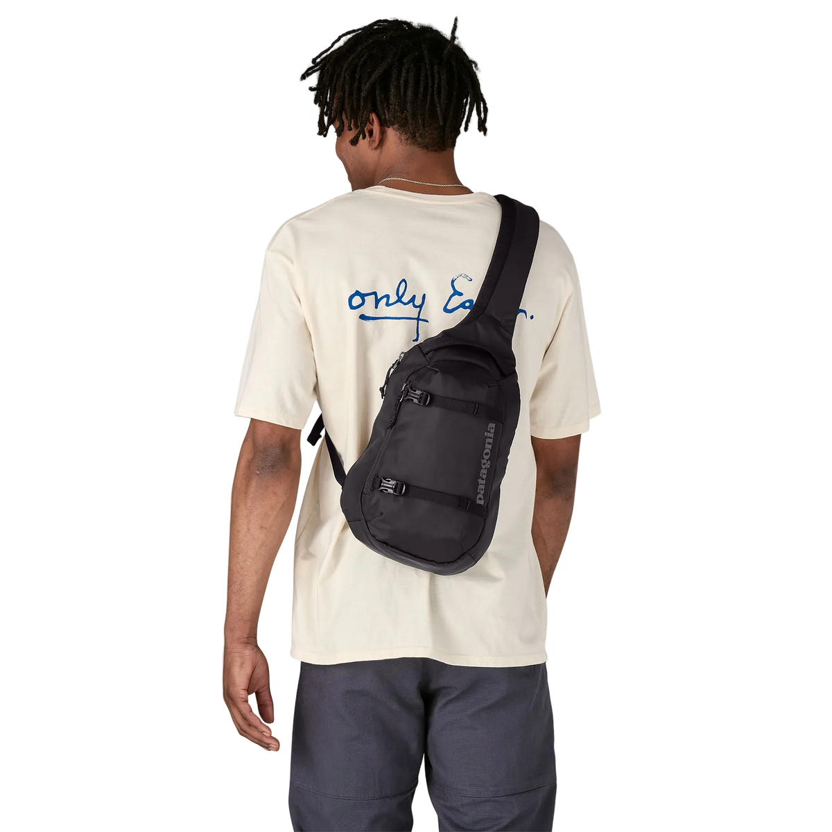 Man wearing a black Patagonia Atom Sling 8L Pack featuring 100% recycled ripstop fabric, an asymmetrical single-strap harness with a zippered phone pocket, breathable spacer-mesh back paneling, front zippered accessory pocket, and exterior tuck-away compression straps.