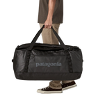 Front view of the black on black Patagonia Black Hole Duffel 100L featuring weather-resistant TPU-laminated ripstop fabric, removable ergonomic backpack shoulder straps, reinforced end haul handles, a padded base, and heavy-duty exterior daisy chain lash loops.