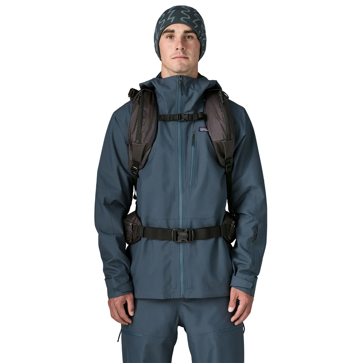 Front view of a black Patagonia SnowDrifter Pack 20L featuring weather-resistant recycled nylon ripstop fabric, diagonal ski and vertical snowboard carry loops, a front avalanche safety gear pocket, fleece-lined top goggle pocket, and shoulder harness accessory pockets.