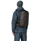 Rear view of a black Patagonia SnowDrifter Pack 20L featuring weather-resistant recycled nylon ripstop fabric, diagonal ski and vertical snowboard carry loops, a front avalanche safety gear pocket, fleece-lined top goggle pocket, and shoulder harness accessory pockets.