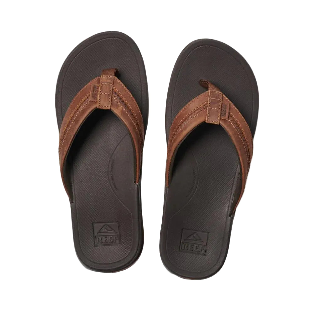 A pair of brown and black Reef Mens Leather Ortho Bounce Coast flip-flop sandals on a white background