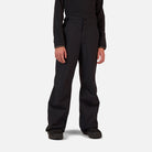 A boy wearing a pair of black Rossignol Boys' Insulated Ski Pants that are waterproof, breathable, and stretchable.