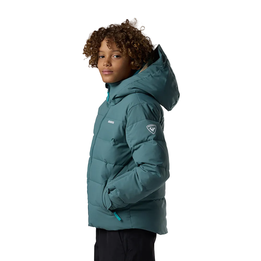 Side view of a blue Rossignol Jr Boys’ Siz Quilted Jacket featuring high-loft synthetic insulation, quilted baffle construction, DWR-treated shell, high stand-up collar, and zippered handwarmer pockets.